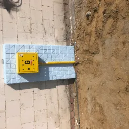 Żółta skrzynka gazowa z oznaczeniem 'G' i podłączoną rurą gazową na jasnej płycie chodnikowej, obok wykopana ziemia.