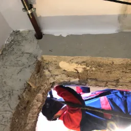 Pracownik w kasku spawalniczym, w trakcie prac instalacyjnych wewnątrz budynku, widoczny fragment instalacji i surowy stan ścian.