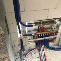 Rozdzielacz ogrzewania podłogowego w metalowej obudowie, widoczne niebieskie i czerwone rury w surowym stanie