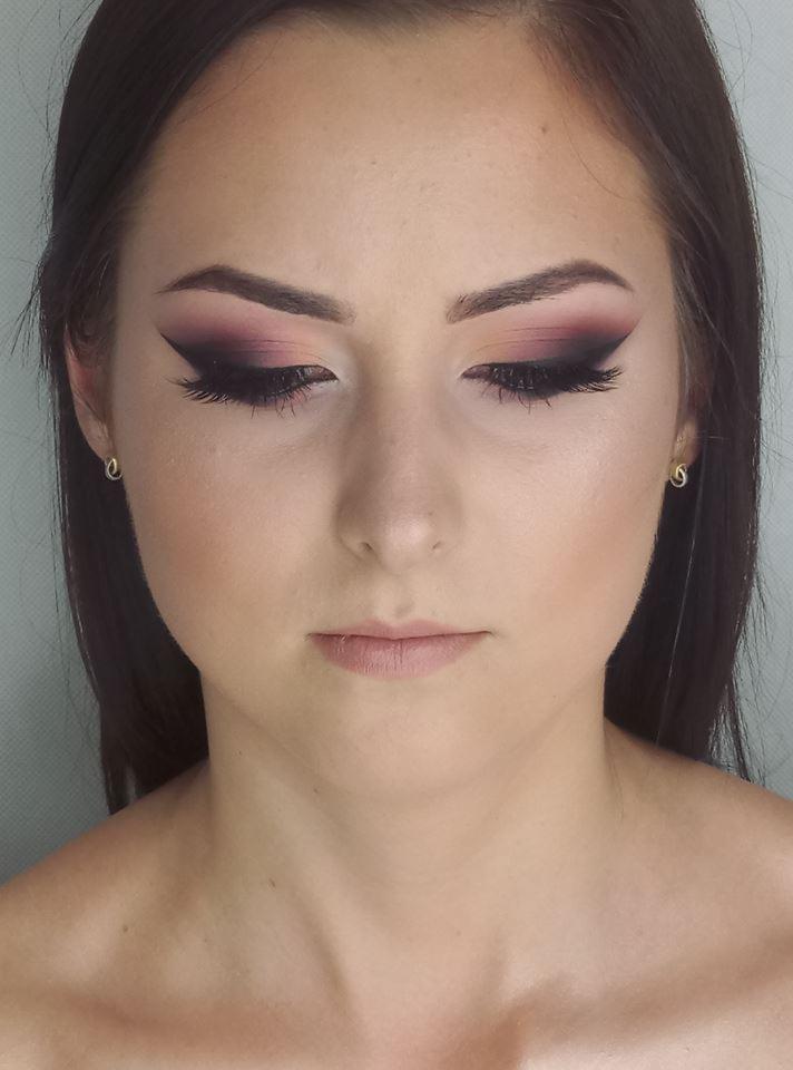 Portret kobiety z profesjonalnym, wieczorowym wizażem: ciemne, przydymione oko z wyraźną, czarną kreską i subtelny makijaż ust. Widoczne delikatne kolczyki.