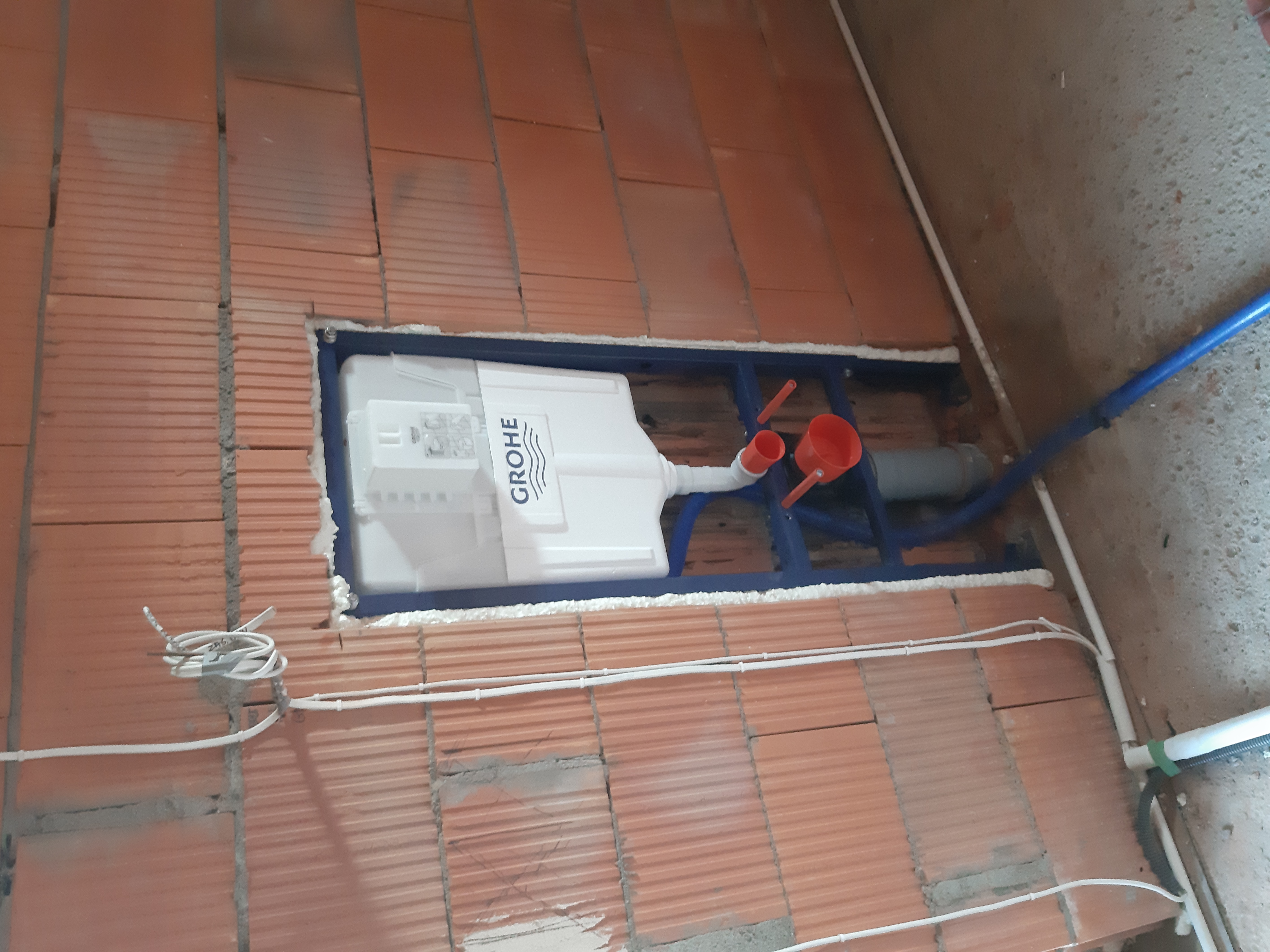 Montaż podtynkowego stelaża WC marki Grohe w ścianie z cegły, widoczne rury doprowadzające wodę i odpływ