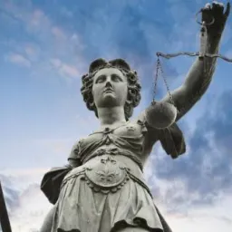 Statuła Temidy z mieczem i wagą sprawiedliwości na tle pochmurnego nieba.