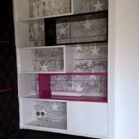 Biała półka z dekoracyjnym tłem w gwiazdy, wkomponowana we wnękę, z fuksjowym akcentem kolorystycznym na jednej z półek, widoczne gniazdka elektryczne.