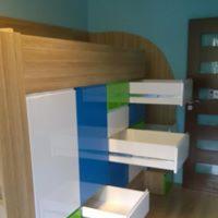 Antresola z biurkiem i szafkami w pokoju dziecięcym, fronty w kolorach białym, niebieskim i zielonym, drewniane wykończenie, widoczne drzwi w tle.