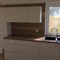 Biała, minimalistyczna kuchnia z drewnianym blatem i panelem ściennym, widok na zewnątrz przez okno, bateria kuchenna z pojedynczym uchwytem