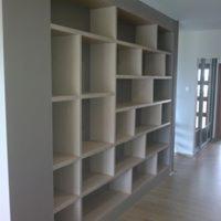 Półki wnękowe z jasnego drewna, asymetryczny układ, szara ściana boczna, widok z boku.