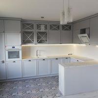 Jasnoszara zabudowa kuchenna w stylu klasycznym z wyspą, oświetleniem LED podszafkowym i dekoracyjnymi frontami górnych szafek z krzyżującymi się listwami, na podłodze wzorzyste płytki.