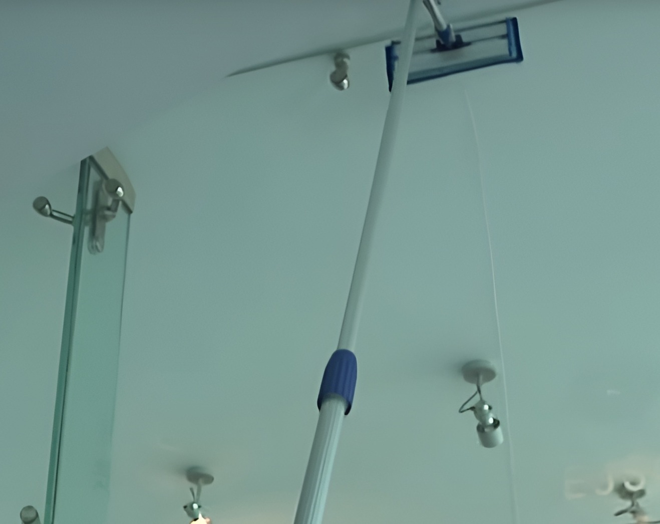 Praca na wysokościach w Gorzowie Wielkopolskim: Mop na teleskopowym kiju czyści szklany sufit z widocznymi punktowymi lampami.