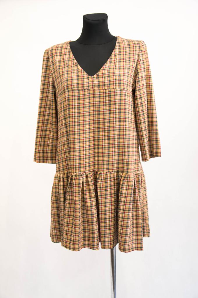 Sukienka w drobną kratę z długimi rękawami i falbaną na dole, prezentowana na czarnym manekinie na tle białej ściany.