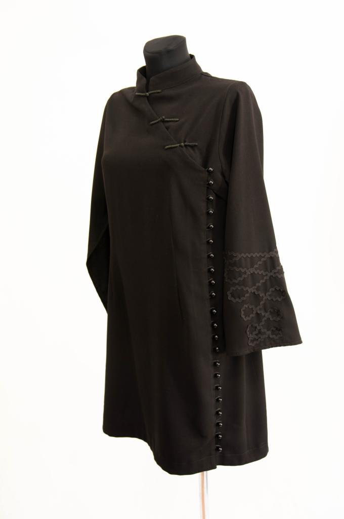 Czarna sukienka w stylu orientalnym na manekinie, z zapięciem na guziki wzdłuż boku i zdobieniami na rękawach.