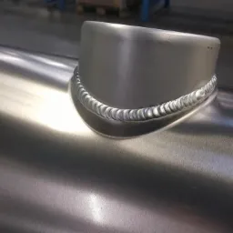 Spoina spawalnicza łącząca rurę z króćcem, widoczna struktura spoiny i powierzchnia metalu.