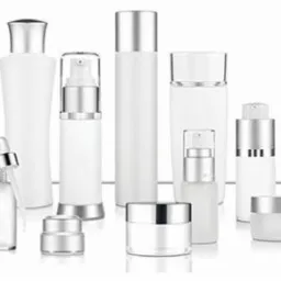 Różnorodne białe, szklane i plastikowe pojemniki kosmetyczne z srebrnymi elementami, w tym butelki z pompkami, pipety i słoiczki, ustawione na białym tle z subtelnym odbiciem.