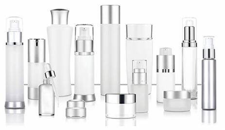 Różnorodne białe, szklane i plastikowe pojemniki kosmetyczne z srebrnymi elementami, w tym butelki z pompkami, pipety i słoiczki, ustawione na białym tle z subtelnym odbiciem.