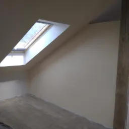 Poddasze po szpachlowaniu i malowaniu na kremowo, widoczne okno dachowe i fragment drewnianej belki konstrukcyjnej.