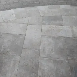 Wyłożony szarymi płytami taras z widocznym fragmentem obrzeża rabaty kwiatowej z kostki brukowej.