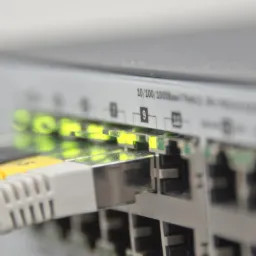 Szczegółowe ujęcie portów Ethernet switcha z podłączonymi kablami (biały i żółty) i świecącymi diodami LED sygnalizującymi aktywność sieciową.