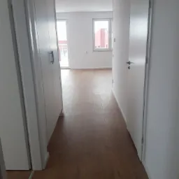 Nowe panele podłogowe imitujące drewno w długim, wąskim korytarzu z białymi ścianami i drzwiami.