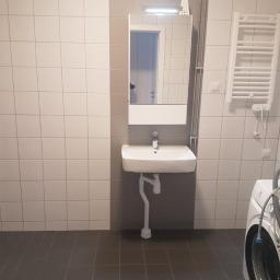 BalBud - Łazienka po remoncie z umywalką nablatową, lustrem z oświetleniem LED, grzejnikiem drabinkowym i pralką. Ściany wyłożone jasnymi płytkami w szachownicę z szarym pasem, podłoga z ciemnych płytek.