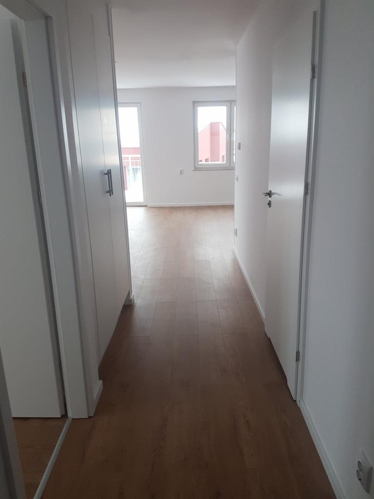 Nowe panele podłogowe imitujące drewno w długim, wąskim korytarzu z białymi ścianami i drzwiami.