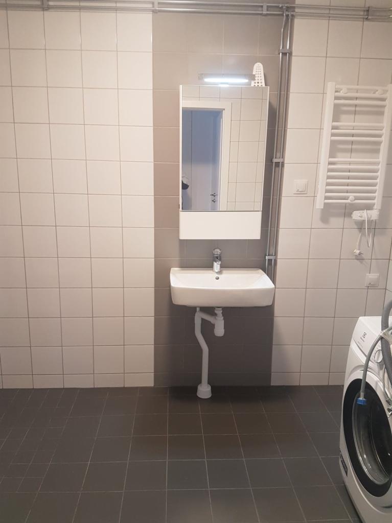 Łazienka po remoncie z umywalką nablatową, lustrem z oświetleniem LED, grzejnikiem drabinkowym i pralką. Ściany wyłożone jasnymi płytkami w szachownicę z szarym pasem, podłoga z ciemnych płytek.