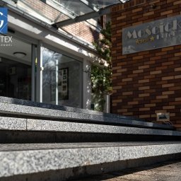 PRZEDSIĘBIORSTWO PRODUKCYJNO HANDLOWO USŁUGOWE „GRANITEX” RESIN SYSTEMS SŁAWOMIR MENDEL - Granitowe schody wejściowe do Hotelu Mościcki, wykonane z kostki granitowej. Widoczny szyld hotelu i logo firmy Granitex. Ujęcie z dołu, podkreślające strukturę kamienia.