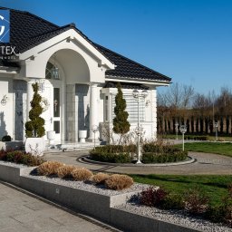 PRZEDSIĘBIORSTWO PRODUKCYJNO HANDLOWO USŁUGOWE „GRANITEX” RESIN SYSTEMS SŁAWOMIR MENDEL - Elegancki dom z granitową elewacją i brukowanym podjazdem. Ozdobne rośliny i lampy kuliste podkreślają estetykę posesji.