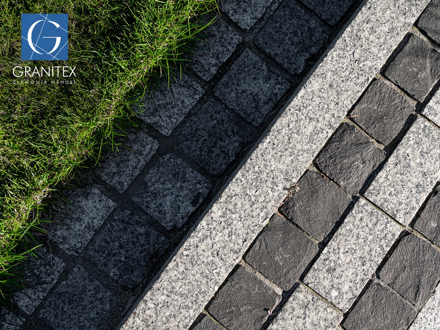 Ułożona kostka granitowa w dwóch odcieniach szarości, oddzielona pasem jaśniejszego granitu, z fragmentem trawy w rogu. Detal nawierzchni.
