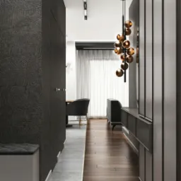 Nowoczesny przedpokój z ciemnymi panelami podłogowymi ułożonymi wzdłuż korytarza, kontrastującymi z szarą wykładziną w strefie wejścia, oraz designerską lampą wiszącą z kulistymi kloszami.