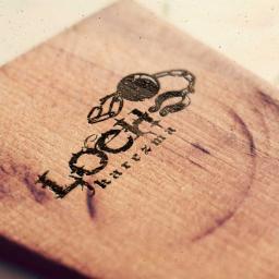 Ambient Studio - Drewniana deska z wygrawerowanym logo firmy i motywem klucza na łańcuszku, widoczne ślady użytkowania.