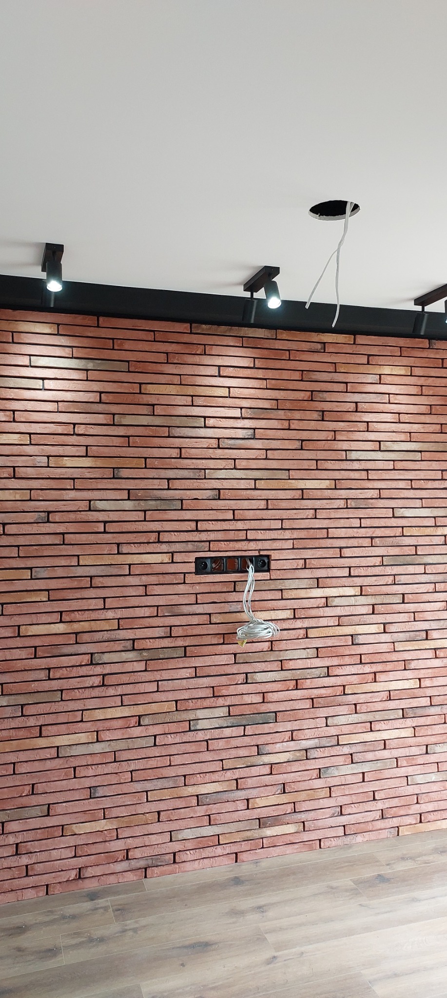 Ściana z cegły klinkierowej z widoczną instalacją elektryczną i oświetleniem punktowym. Wykończenie wnętrza w stylu industrialnym.
