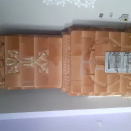 Stylowy piec kaflowy w odcieniach brązu z metalowymi drzwiczkami i zdobieniami kwiatowymi, umieszczony w rogu pomieszczenia, z widoczną dekoracją roślinną na suficie.