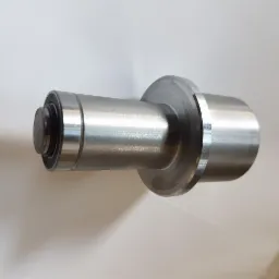 Metalowy wałek z łożyskiem i kołnierzem, obrobiony na tokarce, leżący na białym tle.