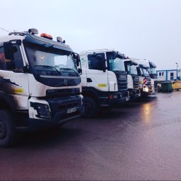 KM Serwis Jakub Michniewski - Szereg zaparkowanych, lekko zabrudzonych ciężarówek Volvo i Scania na mokrym placu, w tle kontener biurowy. Widok z niskiej perspektywy, pochmurna pogoda.