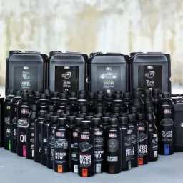 Zestaw czarnych pojemników i butelek z chemią do czyszczenia i pielęgnacji wnętrza samochodu i tapicerki, z grafikami przedstawiającymi elementy auta, na szarym tle.