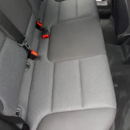 Szare, materiałowe tylne siedzenie samochodowe z widocznymi pasami bezpieczeństwa, po czyszczeniu.