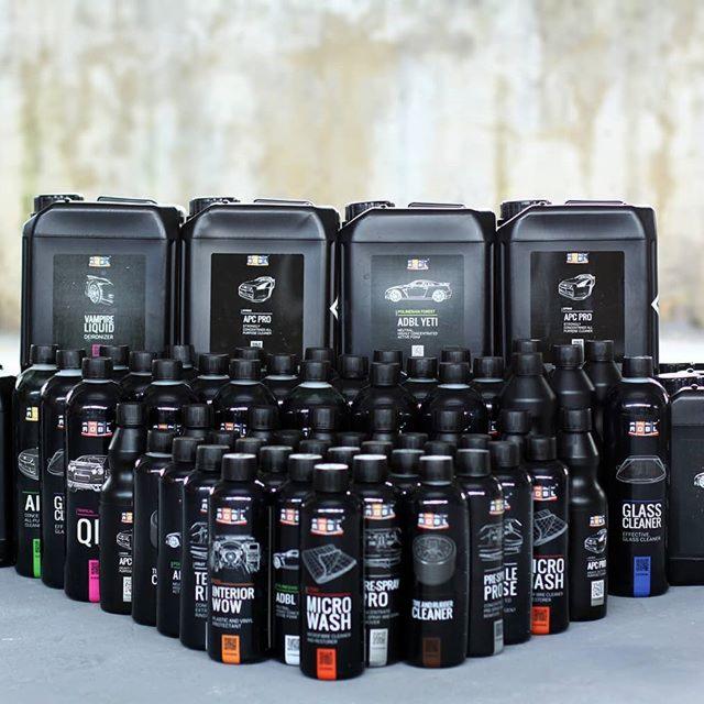 Zestaw czarnych pojemników i butelek z chemią do czyszczenia i pielęgnacji wnętrza samochodu i tapicerki, z grafikami przedstawiającymi elementy auta, na szarym tle.
