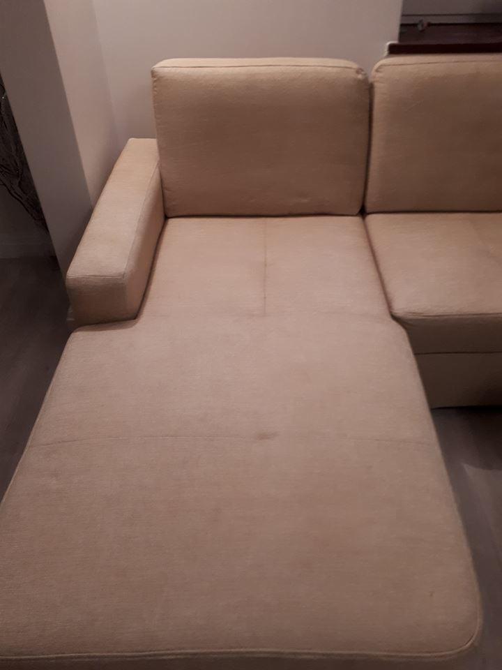 Beżowa, narożna kanapa z widocznymi plamami na siedzisku w słabym oświetleniu.