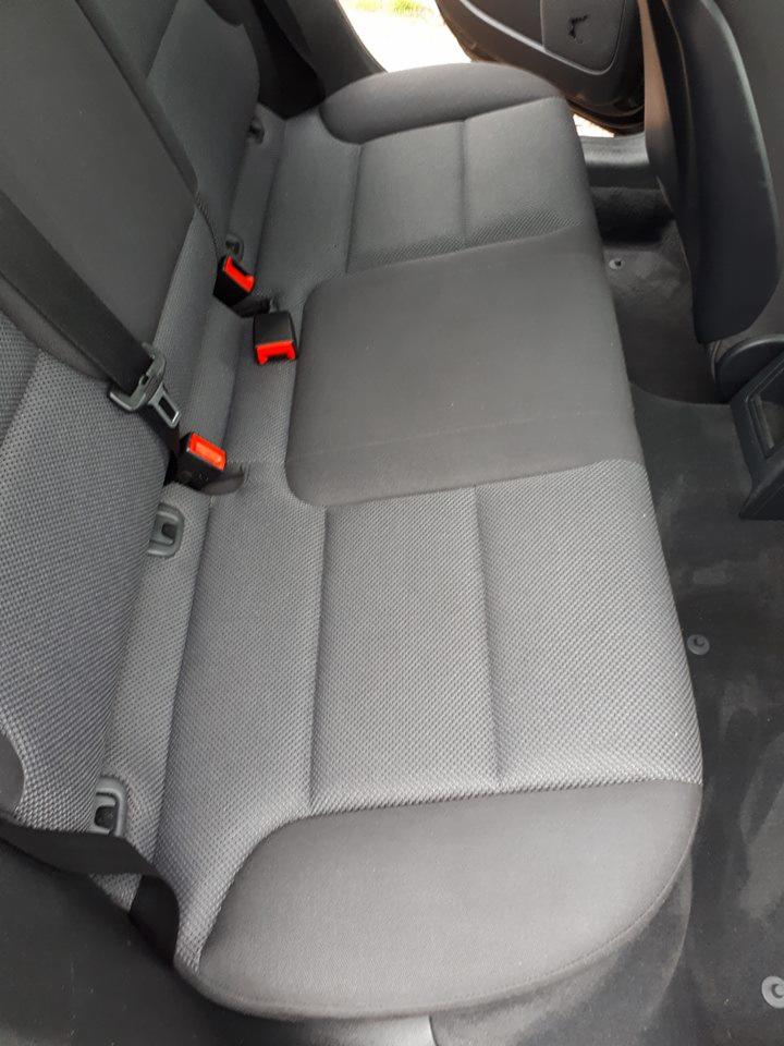 Szare, materiałowe tylne siedzenie samochodowe z widocznymi pasami bezpieczeństwa, po czyszczeniu.