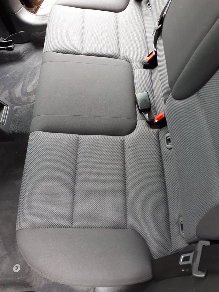Szara, tekstylna tylna kanapa samochodowa z widocznymi pasami bezpieczeństwa i podłokietnikiem, uchwycona z góry pod kątem.