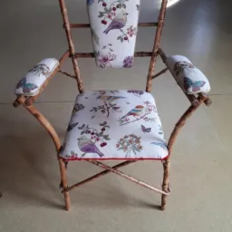 Krzesło z bambusową ramą i tapicerką w motywy ptaków i motyli, zakończone czerwoną lamówką.