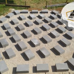 PEP-KOP Roboty Ziemne Usługi Koparko Ładowarką , Minikoparką Wykopy glebogryzarka separacyjna trawniki płyty fundamentowe Różan - Przygotowany teren pod budowę z rozłożonymi bloczkami betonowymi, widoczny piasek, częściowo trawa i logo firmy w prawym górnym rogu.