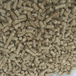 Stos brązowego pelletu ułożonego na worku z białej tkaniny, widoczne nierówności i struktura materiału.