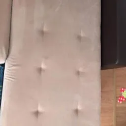 Fragment jasnej, beżowej kanapy z sześcioma wgłębieniami, widoczne ślady czyszczenia, obok fragment brązowej ramy kanapy i drewniana podłoga.