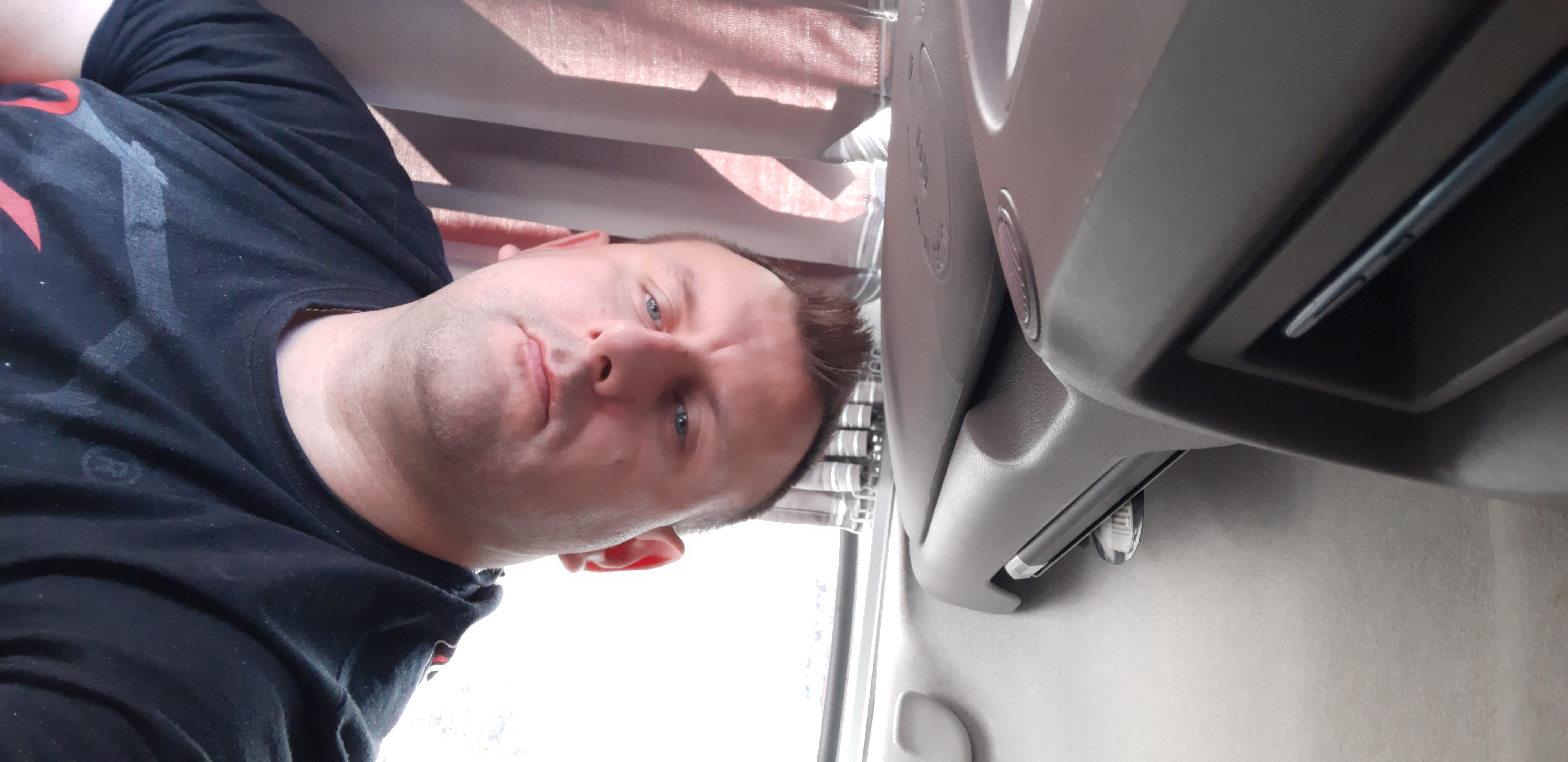 Mężczyzna w czarnej koszulce z nadrukiem, siedzący w kabinie samochodu dostawczego, widok od dołu.