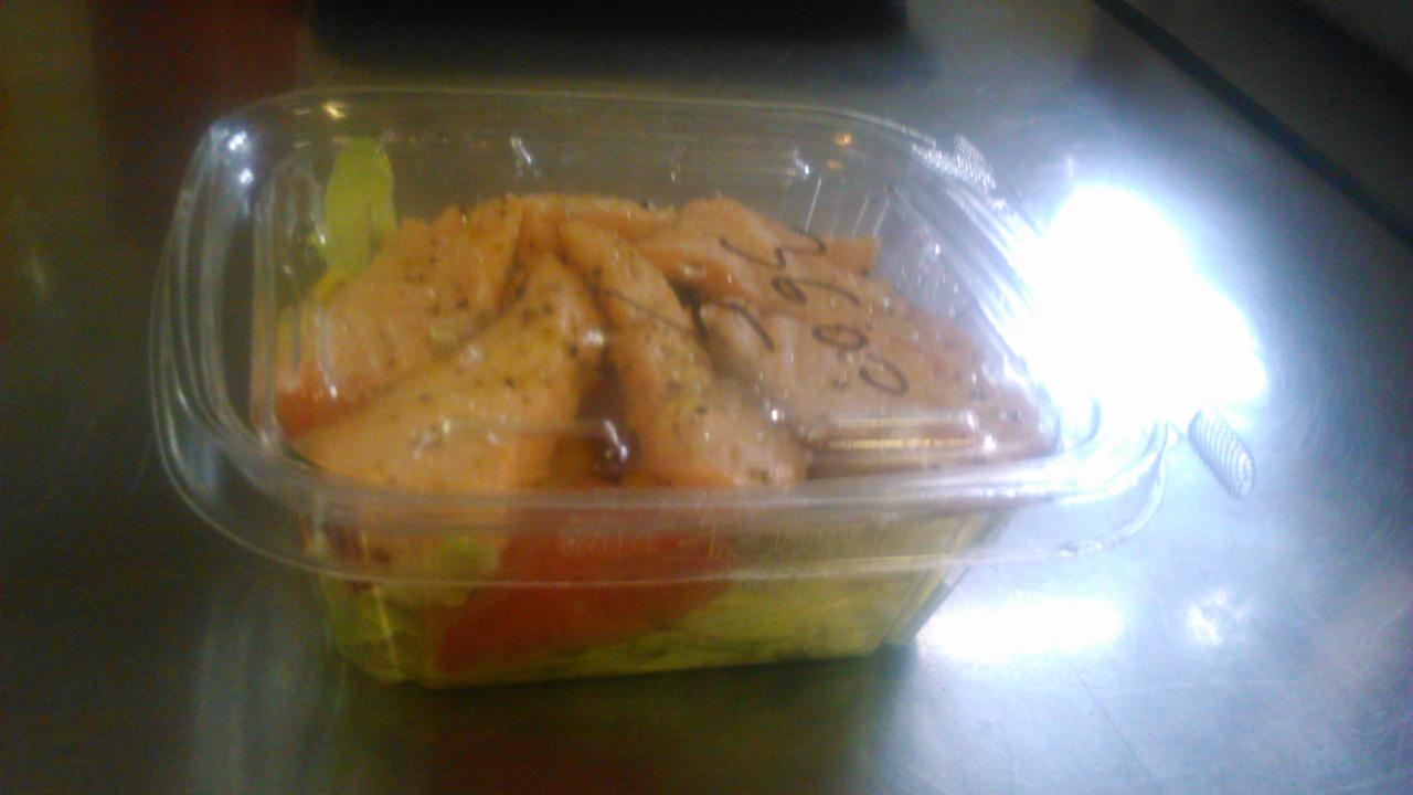 Sałatka z grillowanym kurczakiem, pomidorami i sałatą w plastikowym, przezroczystym pojemniku na metalowym blacie.