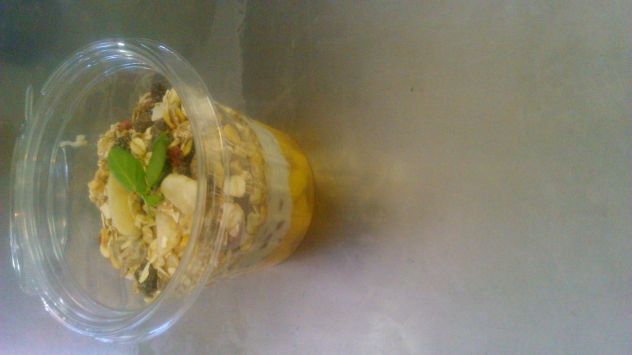 Deser w przezroczystym kubku z warstwami musli, owoców i kremu, udekorowany listkami mięty, leżący na boku na gładkiej powierzchni.