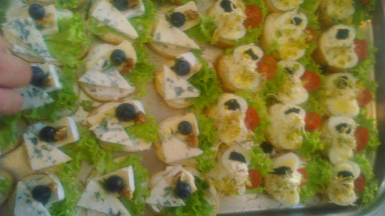 Taca z kanapkami: jedne z serem pleśniowym, orzechami i borówkami, drugie z jajkiem, pomidorem i kiełkami, ułożone na sałacie.