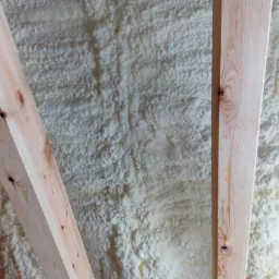 Ściana ocieplona pianką poliuretanową, widoczne fragmenty drewnianej konstrukcji szkieletowej.