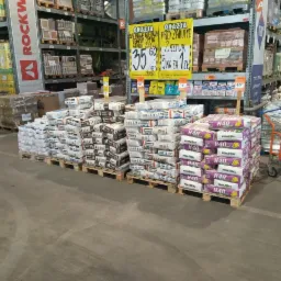 Pakiety zaprawy klejowej Ceresit CM12 i KeraColl H40 ułożone na paletach w składzie budowlanym, promocyjna oferta cenowa widoczna na banerach.