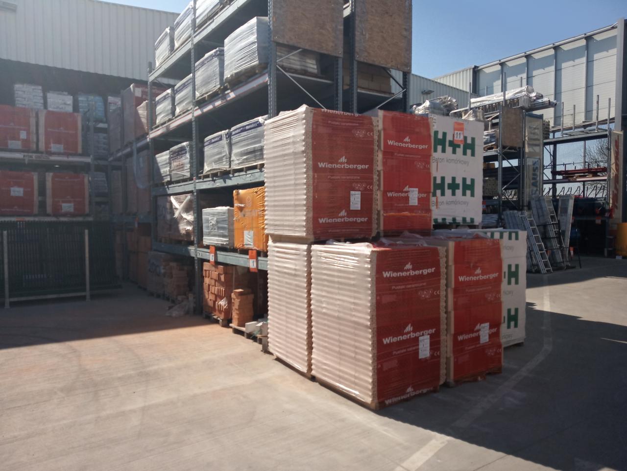 Magazyn budowlany z zapasem cegieł ceramicznych Wienerberger oraz bloczków betonowych H+H ułożonych na paletach i regałach.